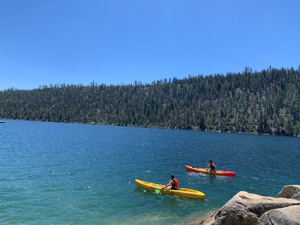 Two people are kayaking on a calm body of water under cloudless skies. 