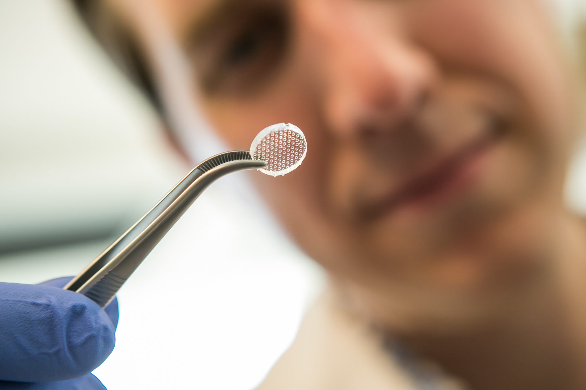 Ben Cosgrove examining tweezers holding clear, circular patch with raised dots
