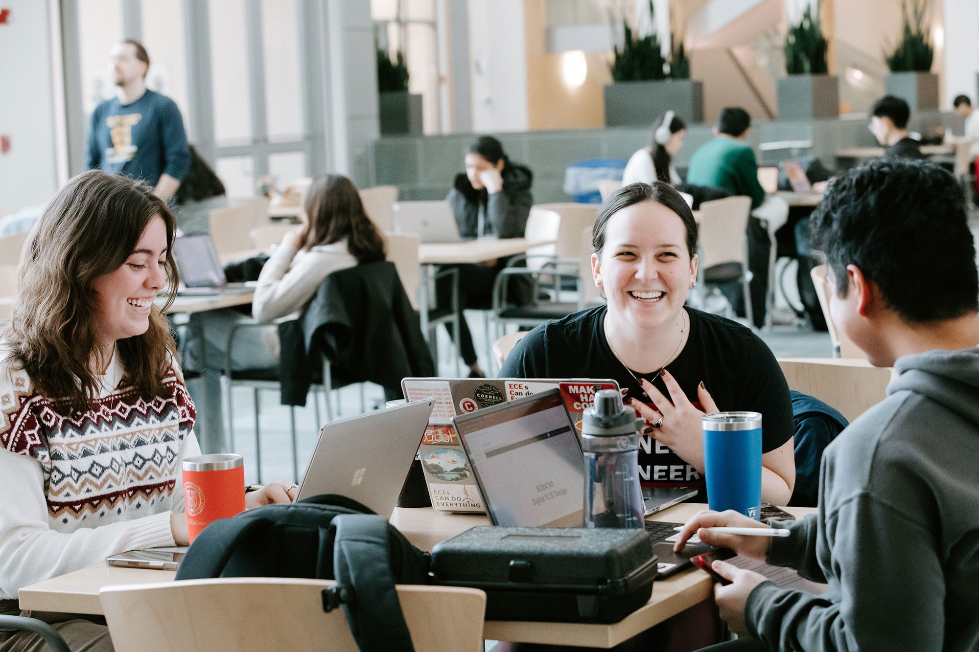 Three students laugh together at table in Duffield Hall
