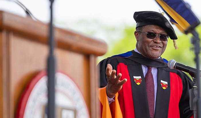 Dean Lynden Archer dressed in academic gown and cap speaks to students