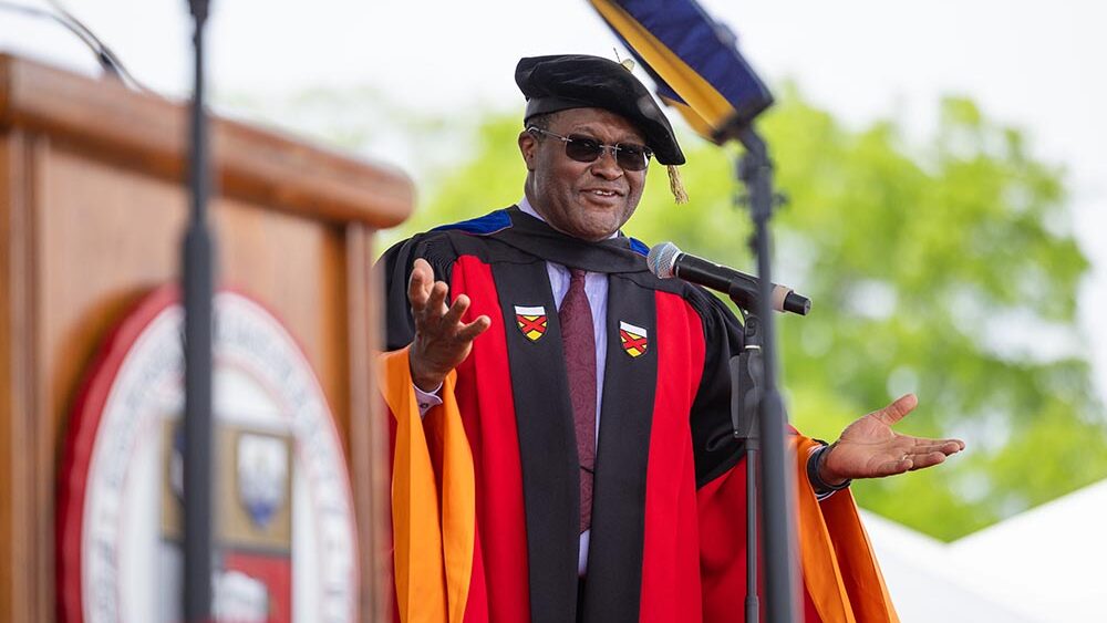 Dean Lynden Archer in academic cap and gown, smiling while speaking on stage