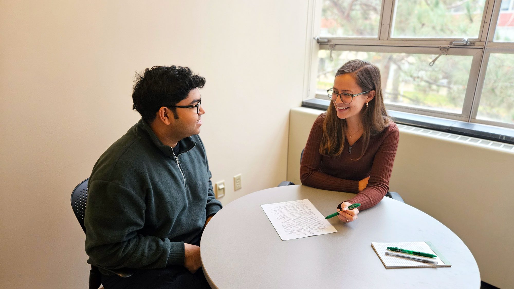 A smiling student works with another student on their resume.