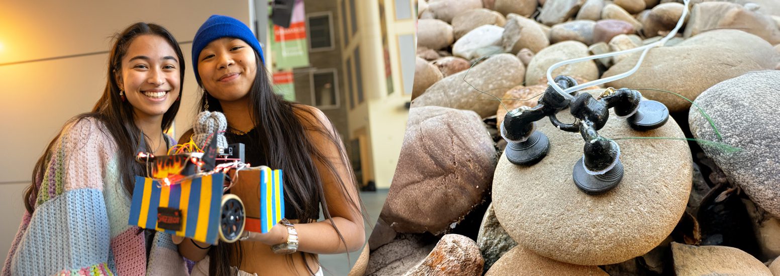 two students hold a wheeled robot, to the left is a small robot perched on a rock