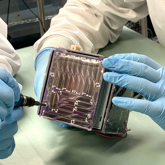 hands solder a small spacecraft shaped like a box