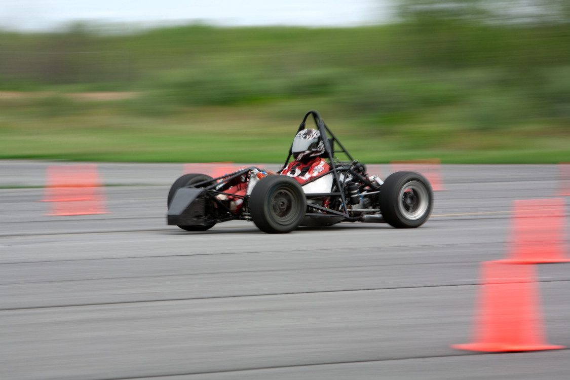 Person wearing helmet drives low, open race car on track