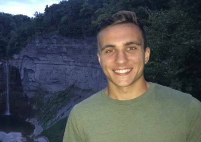 A smiling student stands with a waterfall in the background