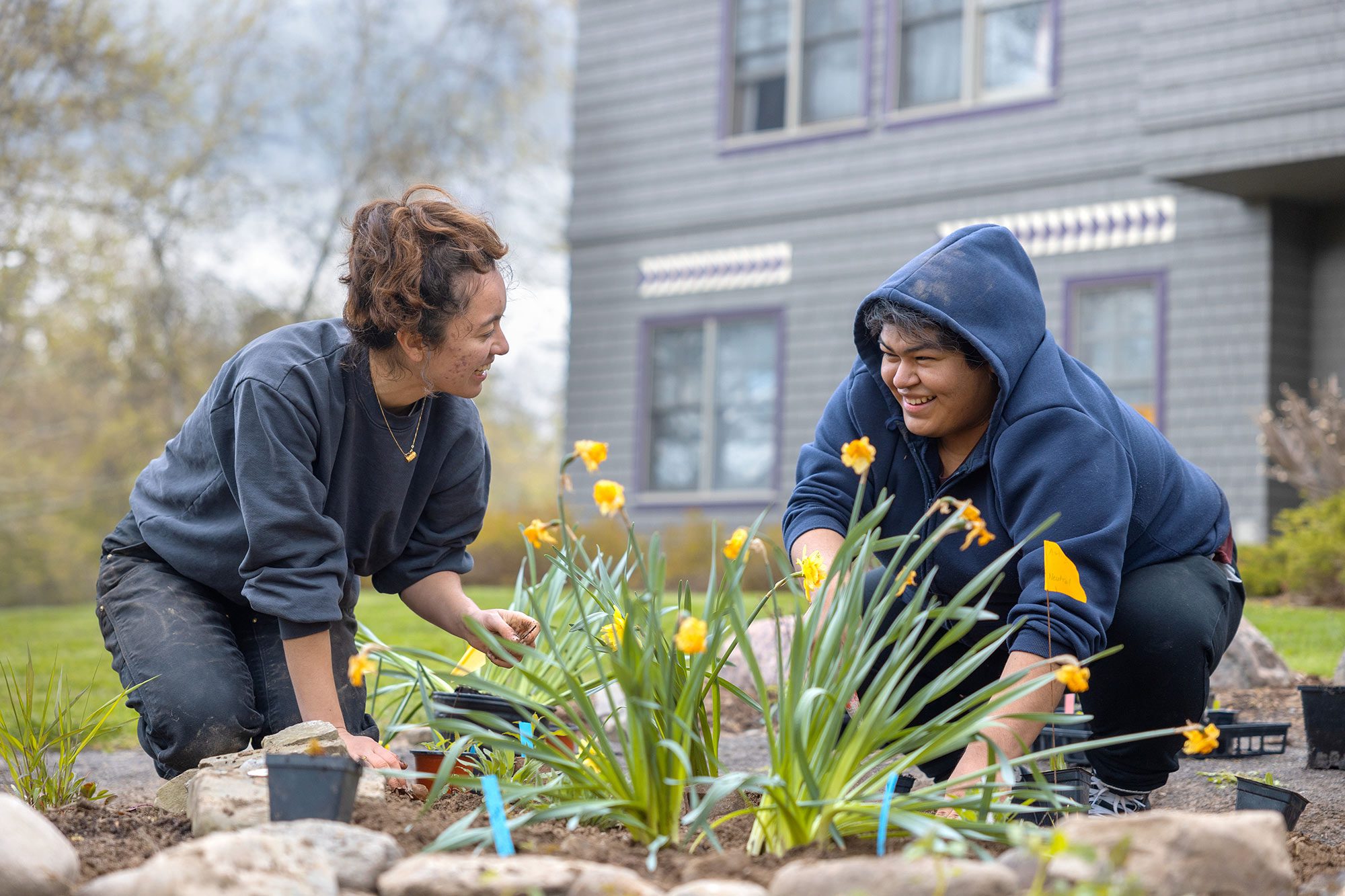Two female students planting daffodils in front of a house and smiling