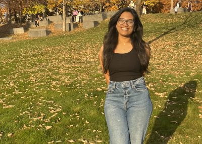 Female student smiling outside on a green lawn with leaves fallen all over