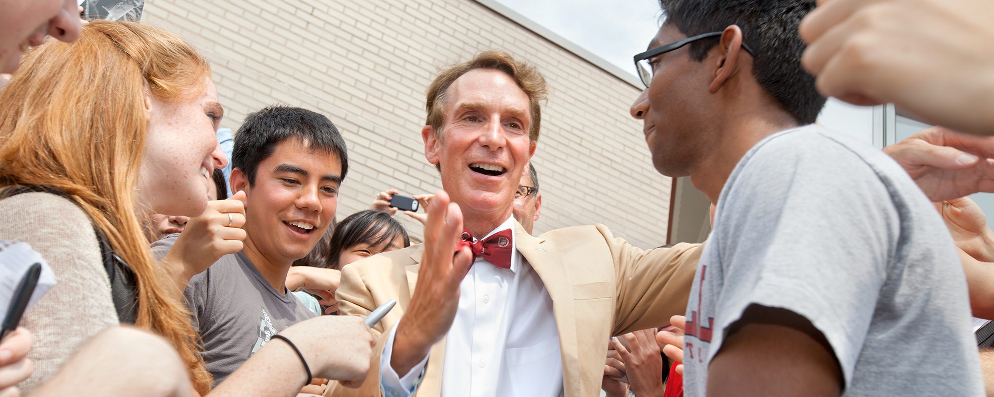 Bill Nye smiling with a crowd of students