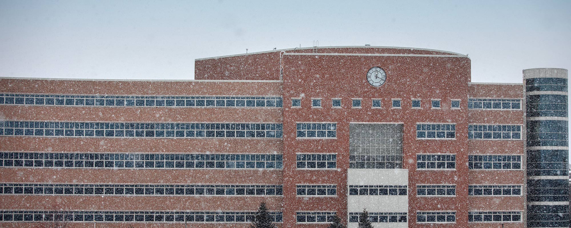 Big modern red building with a clock, as snow falls
