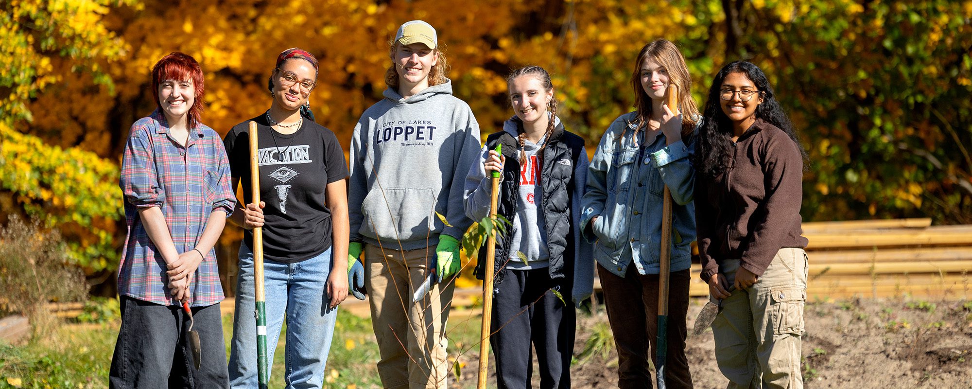 Six students smile for a photo while holding shovels and other gardening equipment during a community outreach project for the sustainable landscapes team