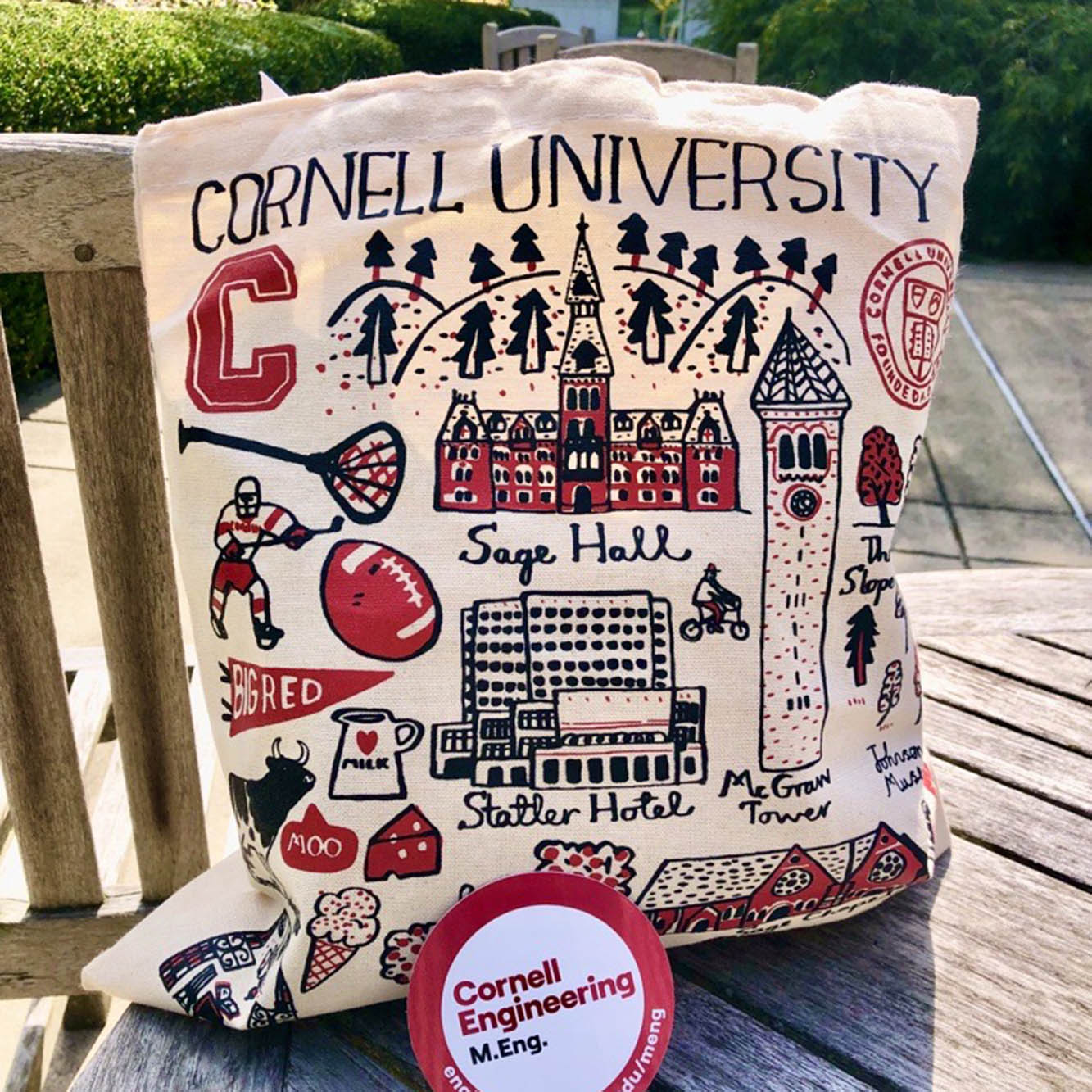 Cornell Tote bag with a sticker for the Cornell Engineering M.Eng. programs sitting on a table outside