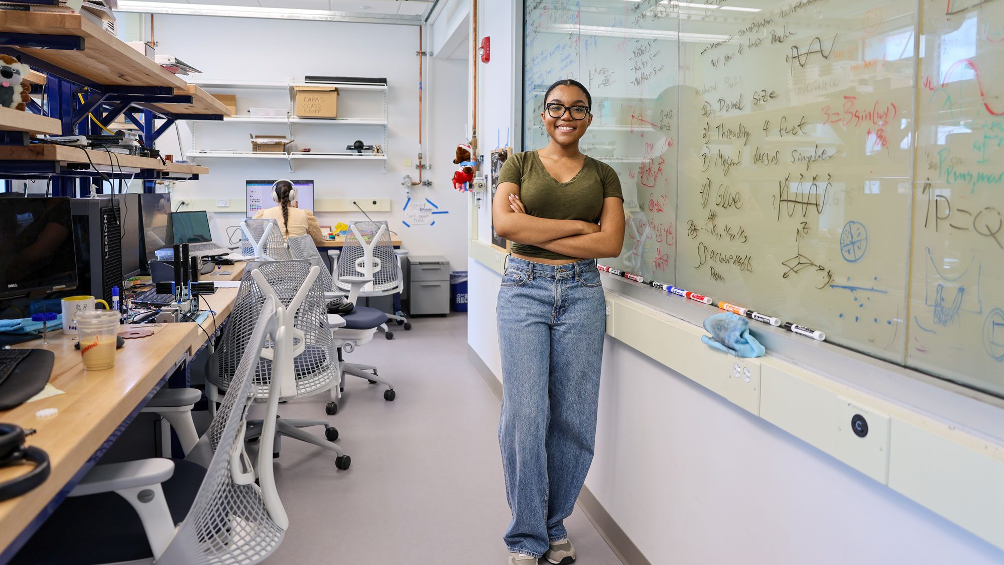 Olivia Tolliver stands by whiteboard with equations and desk with electronics