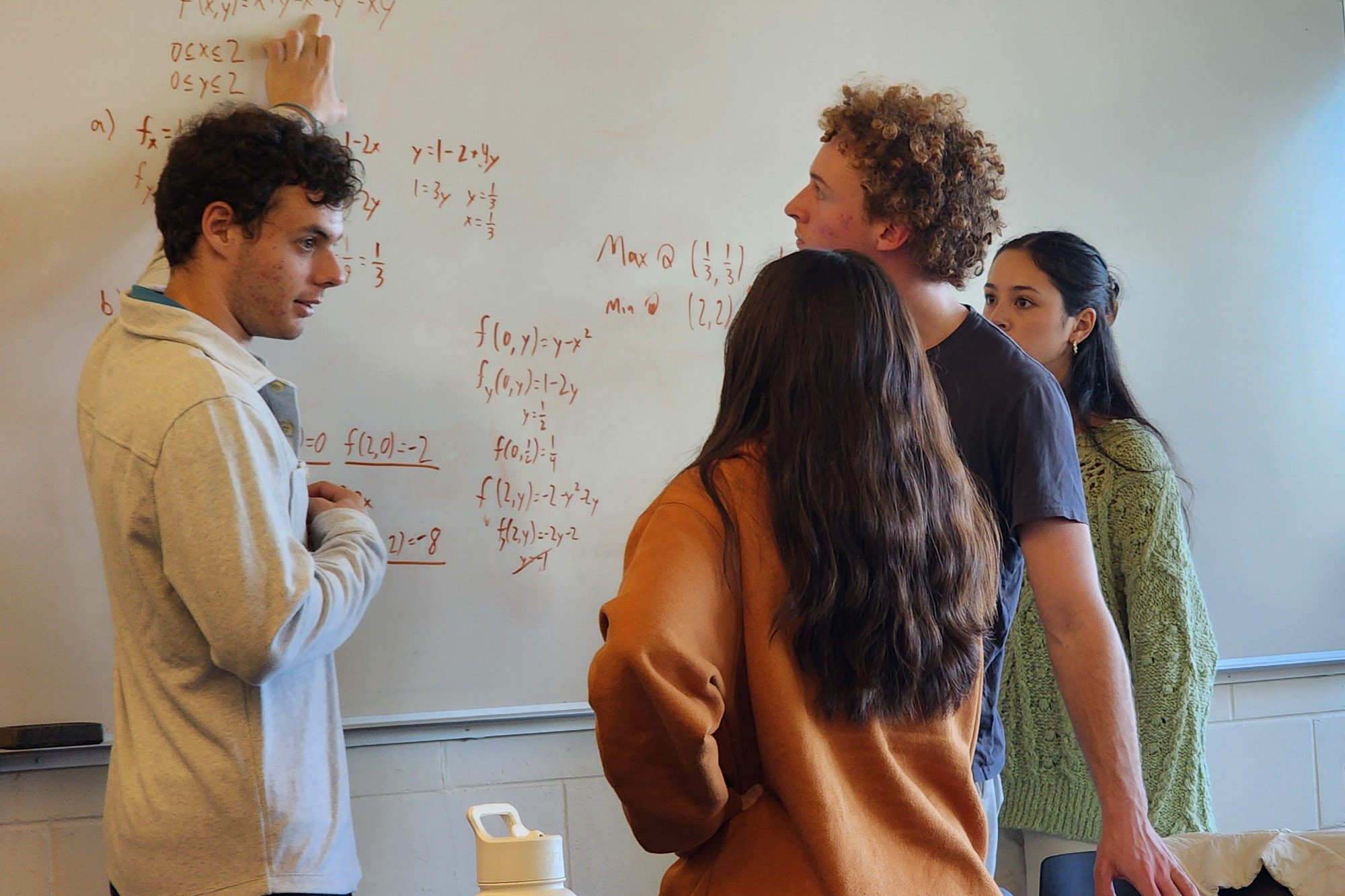 A student leads an academic excellence workshop, talking three peers through equations on a whiteboard